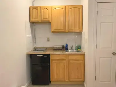 a small kitchen with wooden cabinets and a black dishwasher at Shered bathroom 4 SofaBed + loftbed + kitchen in New York