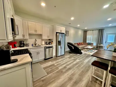 a kitchen with white cabinets and a living room at The Stylish Suite - 1BR with Free Parking in Paterson