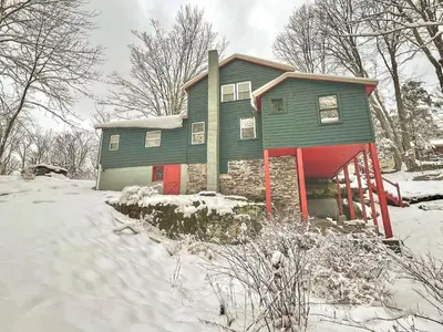 a green house with red doors in the snow at renovatedhot tubnear skiingtubingcozy & chic in Monticello