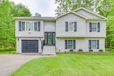 a white house with a garage at 9 Mi to Camelback! Home with Hot Tub and Fire Pit in Long Pond