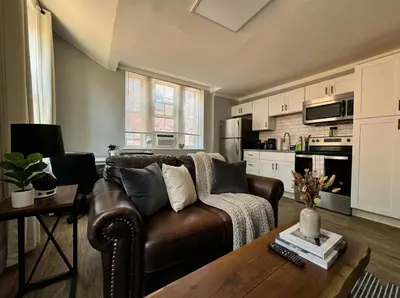 a living room with a brown leather couch and a kitchen at The Grayson at Park Place- cozy and fully updated with King bed free coffee and fast WIFI in Wilmington