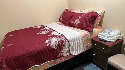 a small bed with a red comforter and a night stand at Room J Divine Villa and Resorts 5mins to EWR Airport and 4mins to Penn Station Newark, New York in Newark