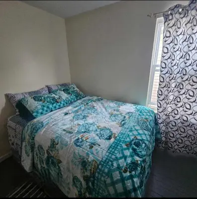 a bedroom with a bed with a blue comforter and a window at Room K Divine Villa and Resorts 5mins to EWR Airport and 4mins to Penn Station Newark, New York in Newark