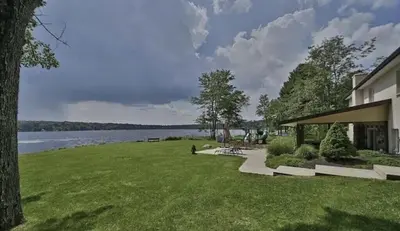a building with a grassy yard next to a lake at Hideaway - LakeHouse/spa/dock/ in Pocono Summit
