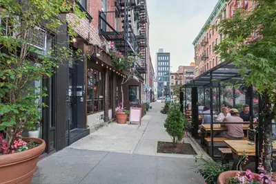 a city street with people sitting at tables on a sidewalk at Classic LES 1br w wd nr SoHo NYC-646 in New York
