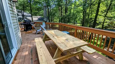 a wooden picnic table on a deck with a grill at The Bear Foot Lodge by AvantStay Game Room Deck BeachLake Access in Albrightsville