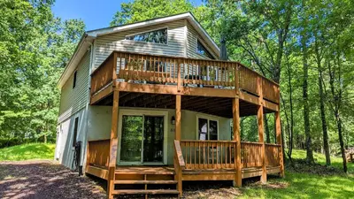 a house with a wrap around deck in the woods at The Bear Foot Lodge by AvantStay Game Room Deck BeachLake Access in Albrightsville