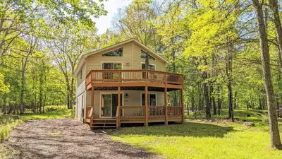 a house with a wrap around deck in the woods at The Bear Foot Lodge by AvantStay Game Room Deck BeachLake Access in Albrightsville