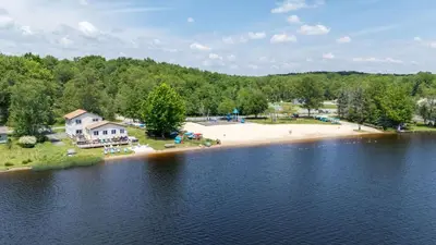 an aerial view of a beach and a house on the water at The Lake Life by AvantStay Lakefront View Hot Tub in Arrowhead Lake