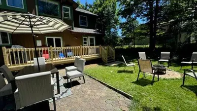 a patio with chairs and an umbrella in front of a house at The Wooden Nest by AvantStay Deck Big Yard w Hammocks Fire Pit in Long Pond