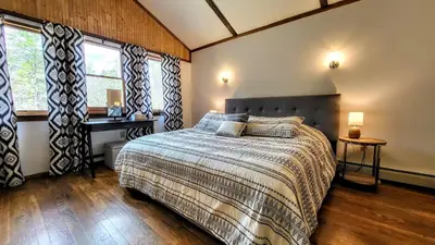a bedroom with a bed and a desk and windows at The Wooden Nest by AvantStay Deck Big Yard w Hammocks Fire Pit in Long Pond