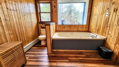a bathroom with a tub and a toilet and a window at The Wooden Nest by AvantStay Deck Big Yard w Hammocks Fire Pit in Long Pond
