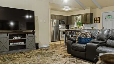 a living room with a black leather couch and a television at Frolic on Fern by AvantStay Enclosed Deck w Forest Views Bar in Blakeslee