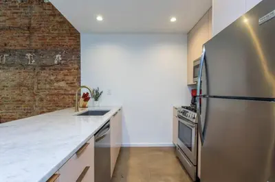 a kitchen with a stainless steel refrigerator and a brick wall at Inventors' Loft - Stay in the Heart of it All in Philadelphia