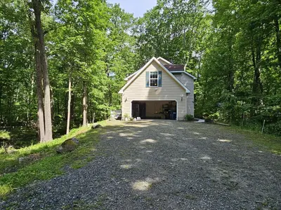 a white house with a garage in the woods at 30 Day Minimum Stay - Private Creekside Solace in East Stroudsburg