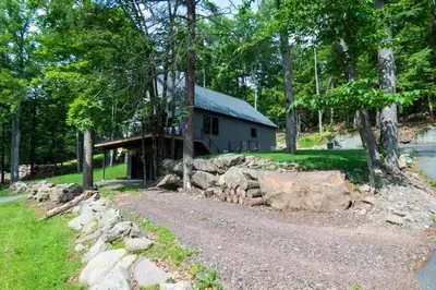 a house in the woods with a gravel road in front at Modern Chalet with Hot Tub and Lake Access in Monticello