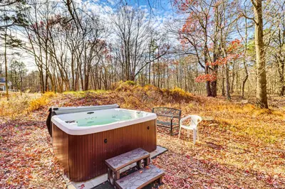 a hot tub and a chair in the woods at Serene Poconos Cabin with Hot Tub and Beach Access! in Albrightsville