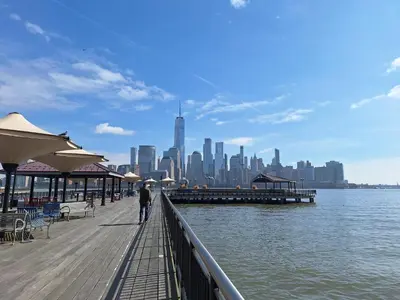 a man standing on a pier with a view of the city at NYC HomeBnB in Jersey City