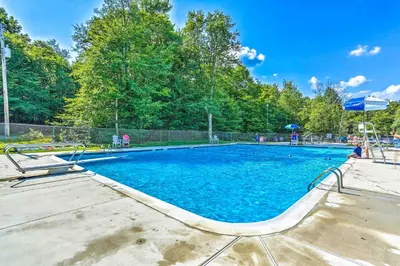 a large swimming pool with blue water and trees at Pocono Lake House Hideaway Hot Tub and Theater Room in Pocono Lake