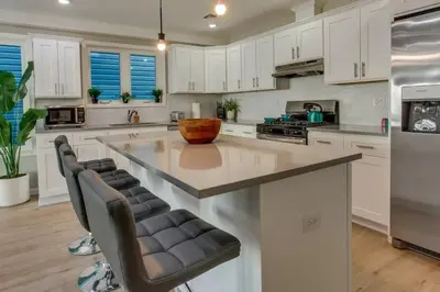 a kitchen with white cabinets and a large island with bar chairs at Modern City Getaway Near Downtown Newark & NYC in Newark