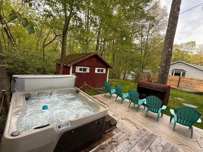 a hot tub on a deck with chairs and a house at Bear Run Bungalow in Hawley