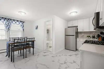 a white kitchen with a table and a refrigerator at Comfy Cozy retreat - NYC & NWK w free parking in Bayonne