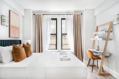 a white bedroom with a large bed and a chair at 73-318 New Studio UWS Doorman Gym in New York