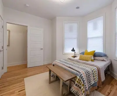 a bedroom with a bed with a table and two windows at Modern & Spacious 3 BED & 2 BA Condo mins from NYC in Jersey City