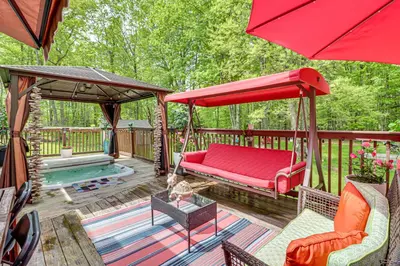 a porch with a red couch and umbrella and a pool at Long Pond Home with Hot Tub about 8 Mi to Kalahari! in Long Pond