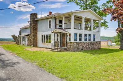 an old stone house with a porch on a lawn at Wellsboro Farmhouse with Grill and Fire Pit! in Wellsboro