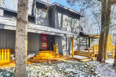 a house with a red door in the snow at Creek Access and Deck Family Pocono Pines Cottage in Pocono Pines