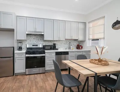 a kitchen with white cabinets and a table with chairs at 25 mins to Midtown Manhattan in Guttenberg
