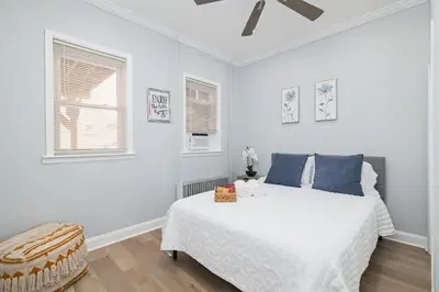 a white bedroom with a large bed with blue pillows at 25 mins to Midtown Manhattan in Guttenberg