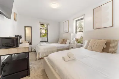 a white bedroom with two beds and a television at Bay Ridge ApartHotel in Brooklyn