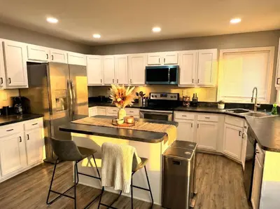 a kitchen with white cabinets and a kitchen island with chairs at Cozy Modern Villa in New Castle