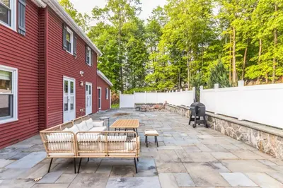 a patio with couches and a grill next to a red building at Enchanting Historic Home near West Point Beacon in Cornwall-on-Hudson