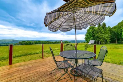 a table and chairs on a wooden deck with an umbrella at Secluded Oxford Cabin on 75 Acres Sunset Views! in Oxford