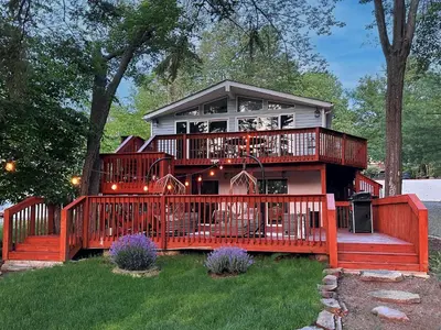 a house with a large deck with a balcony at Majestic Lake Front Chalet in Tobyhanna