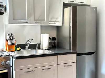 a kitchen with white cabinets and a stainless steel refrigerator at West Village Lush Green in New York