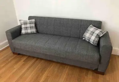 a gray couch with two pillows on a wooden floor at Spacious 2-bedroom apartment with 1-bathroom and private street entrance, MetLife Stadium FIFA World Cup 25 minutes away in Paterson