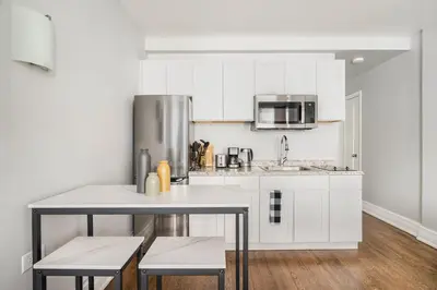 a kitchen with white cabinets and a table and chairs at 73-703 New Studio UWS Doorman Gym in New York