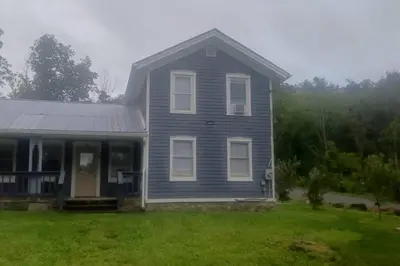 a blue house with a porch and a grass yard at Old farmhouse with Hot tub in the Finger Lakes in Horseheads