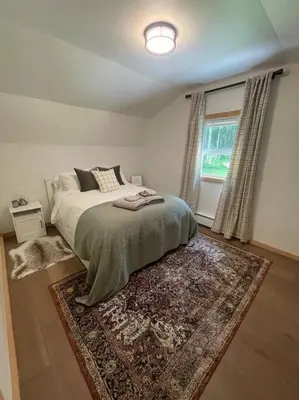 a bedroom with a bed with a rug and a window at Private Cottage with Hot Tub in the Woods in Thompson