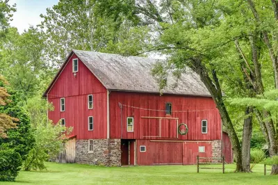 a red barn in a field with trees at Steps to Delaware Canal Enchanting Stone Cottage! in Kintnersville