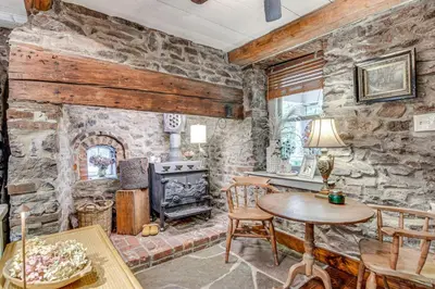 a living room with a stone wall with a stove at Steps to Delaware Canal Enchanting Stone Cottage! in Kintnersville