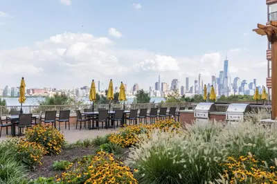a garden with chairs and umbrellas and a city at Global Luxury Suites at Hoboken Waterfront in Hoboken