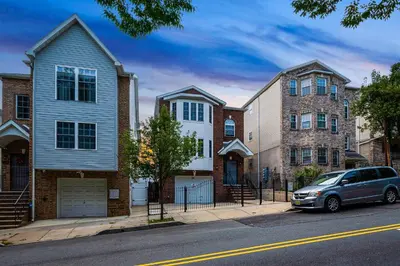a car parked in front of houses on a street at Newark Gem Ruby 3BR, 3BA - Sleeps 14 - Walk to Prudential Center and Newark Penn Station, Near EWR and American Dream Mall, includes Parking - WiFi - Laundry - Backyard - Gym in Newark