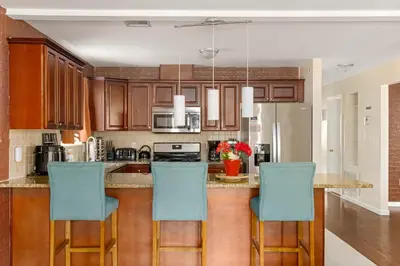a kitchen with wooden cabinets and blue bar stools at Newark Gem Ruby 3BR, 3BA - Sleeps 14 - Walk to Prudential Center and Newark Penn Station, Near EWR and American Dream Mall, includes Parking - WiFi - Laundry - Backyard - Gym in Newark