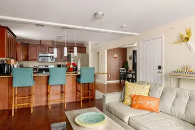 a living room with a couch and a kitchen at Newark Gem Ruby 3BR, 3BA - Sleeps 14 - Walk to Prudential Center and Newark Penn Station, Near EWR and American Dream Mall, includes Parking - WiFi - Laundry - Backyard - Gym in Newark