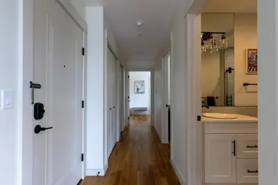 a hallway leading to a bathroom with white walls and wood floors at Downtown Princeton Chic in Princeton